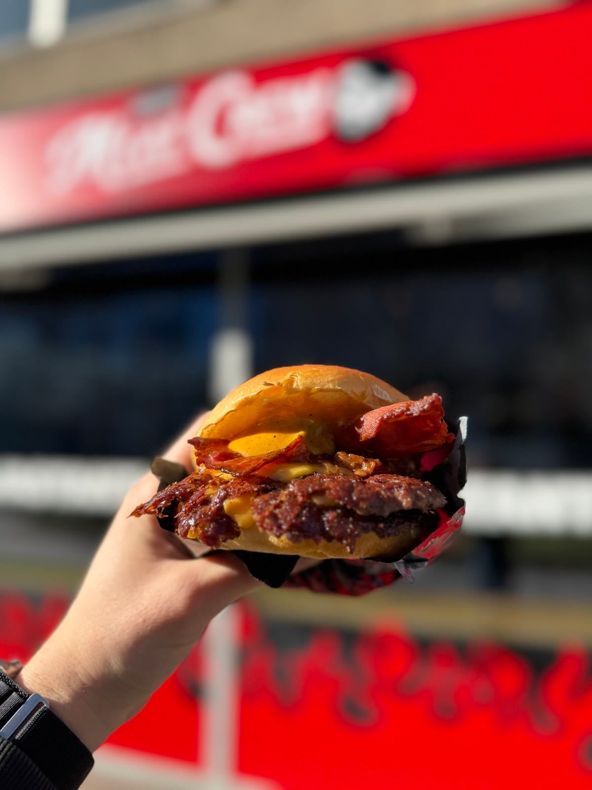 Un burger col bacon davanti all'insegna di Meat Crew in Viale Restelli, a Milano